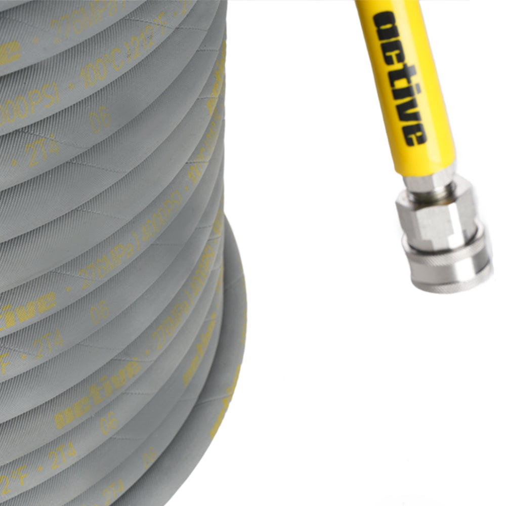 Close-up of an Active™ 50’ Pressure Washer Extension Hose – 5/16 from Active Products Inc., showcasing its grey, coiled design with yellow text on the surface. The durable steel braided construction is visible as the hose connects to a metal fitting, with another yellow section displaying the word "active". The background is white.